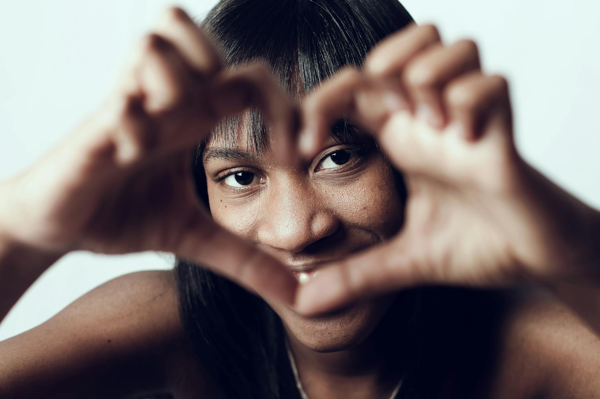 Close-up of a smiling woman creating a heart shape with her hands, expressing love and happiness.